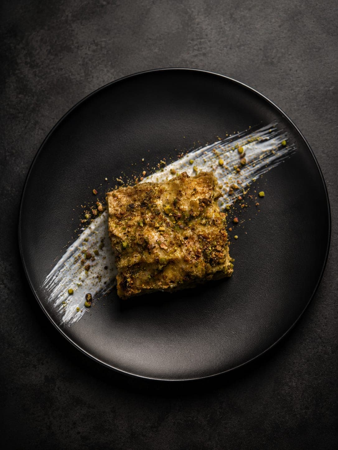 Pistachio-topped dessert on a black plate from a Zagara Dining dinner